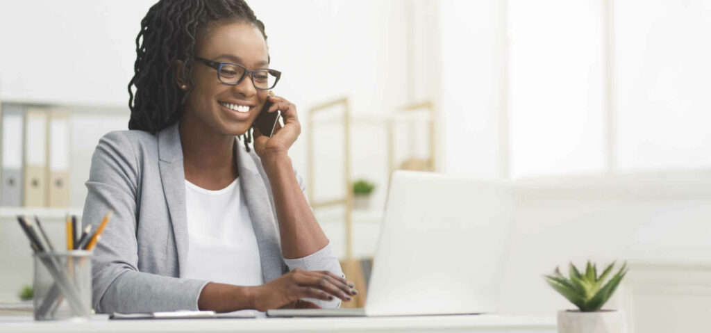 Lady Boss. Afro Businesswoman Talking On Cellphone While Working On Laptop In Modern Office, Wide Horizontal Banner, Panorama With Free Space